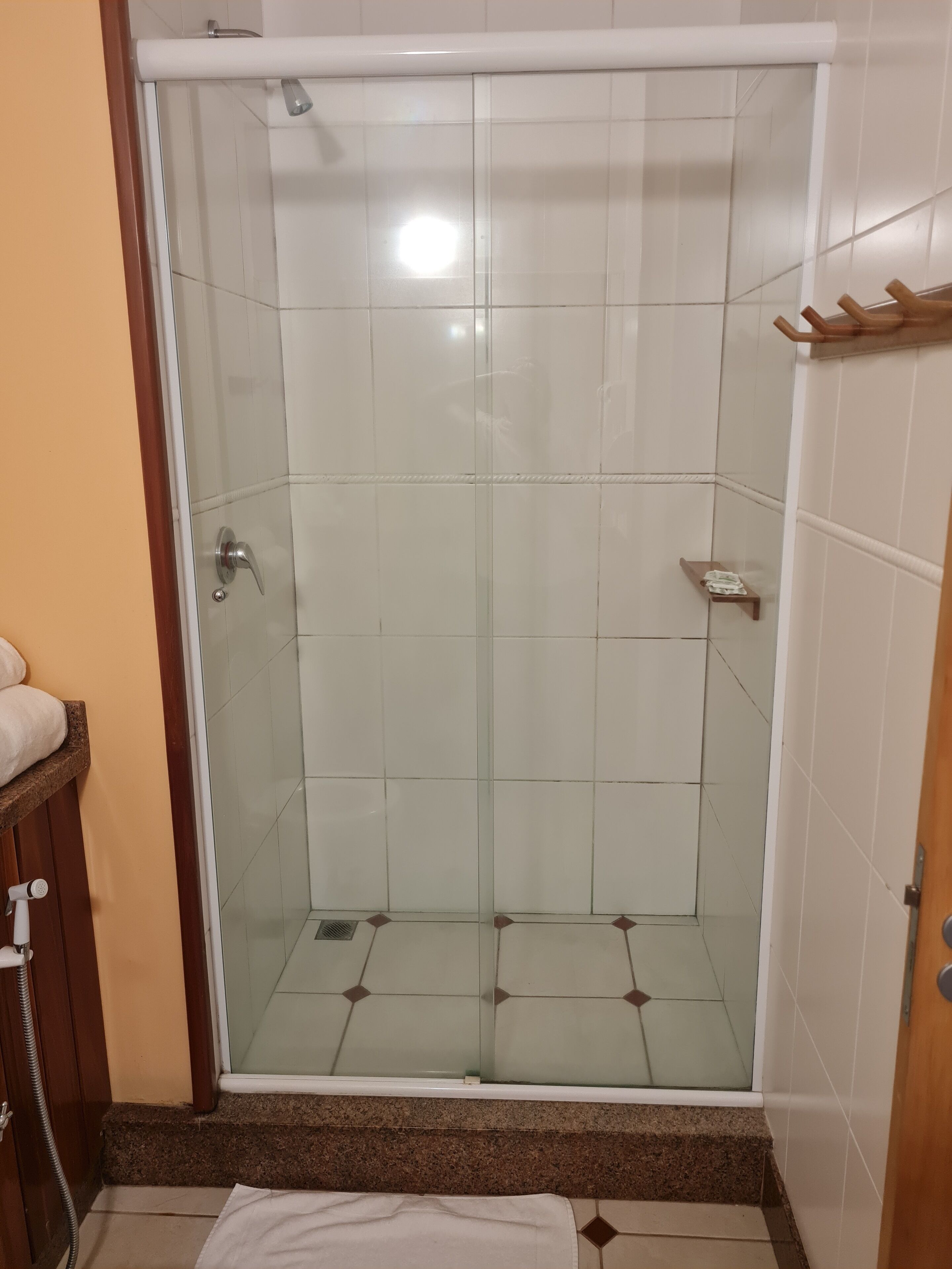 A glass-enclosed shower with a white tiled interior, a wooden shelf, and a towel rack.