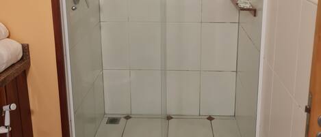 A glass-enclosed shower with a white tiled interior, a wooden shelf, and a towel rack.