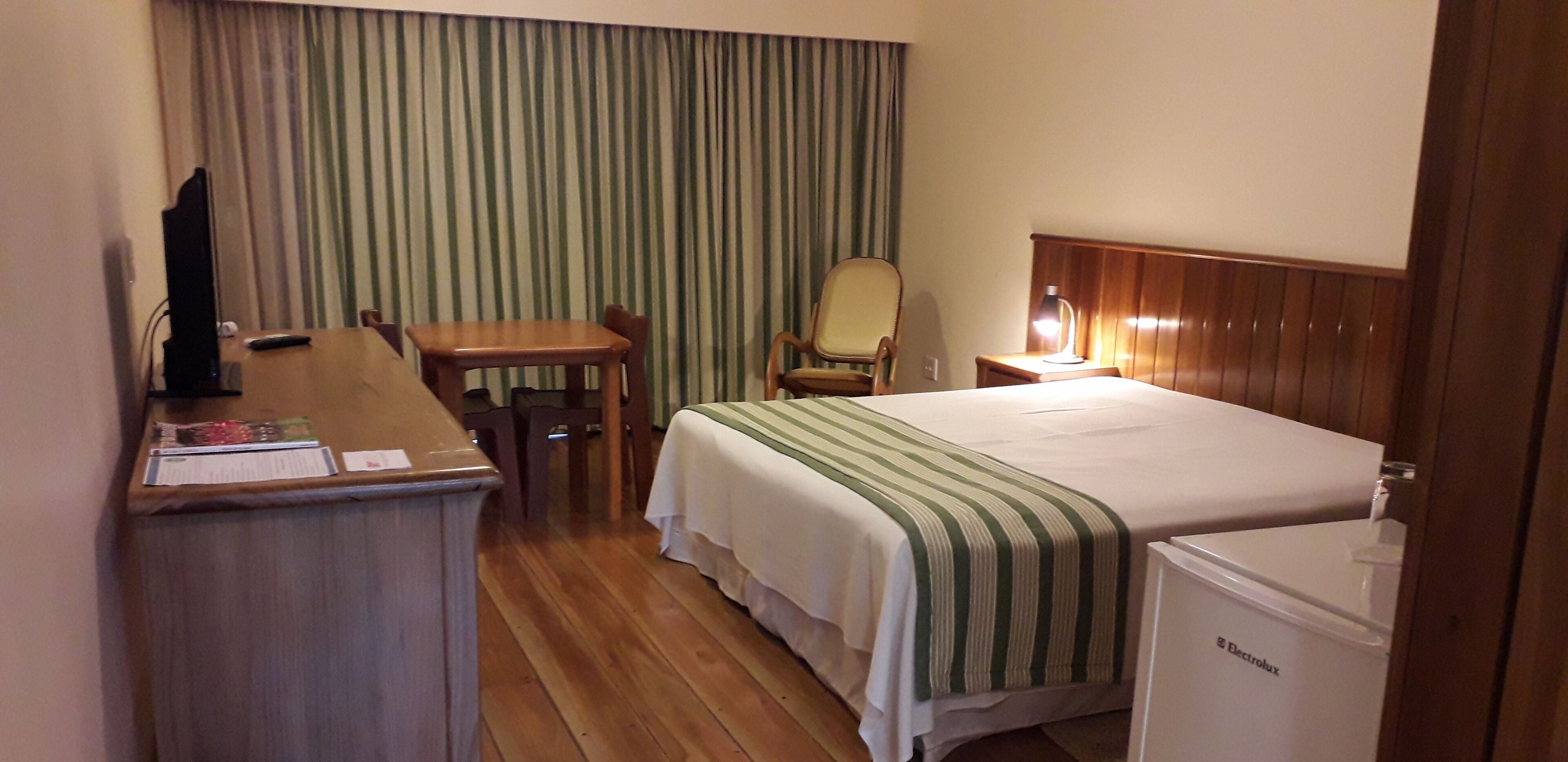 Habitación de hotel con cama, escritorio, silla, televisor y refrigerador.