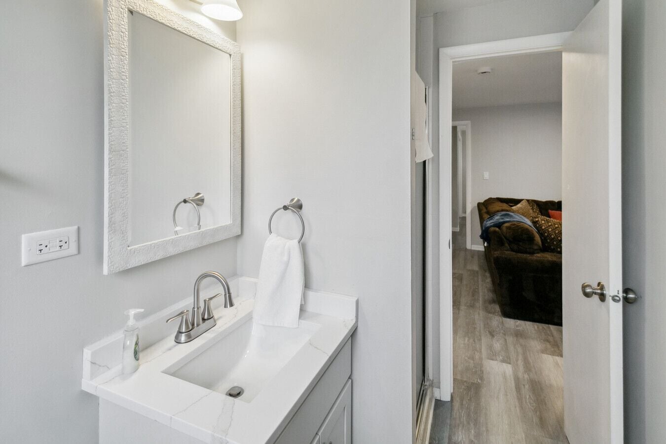 A modern bathroom with a white sink, a large mirror, and a towel ring.