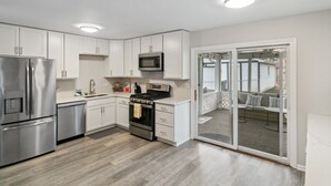 Cocina moderna con armarios blancos, electrodomésticos de acero inoxidable y un puerta corrediza de vidrio que da a un balcón con mobiliario exterior.