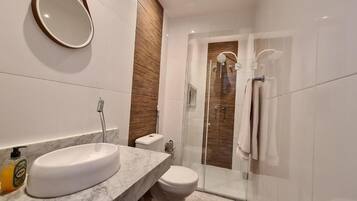 A modern bathroom with a marble sink, a toilet, and a glass-enclosed shower.