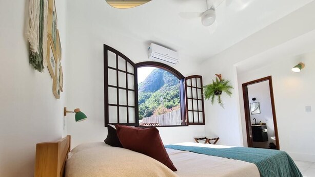 Ein Schlafzimmer mit einem Bett, einem Fenster mit Bergblick, einer Pflanze und einer Tür.