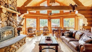 A log cabin interior with a stone fireplace, wooden furniture, and large windows. - San Diego’s Luxury Mountain Cabin Retreat (El Cajon)