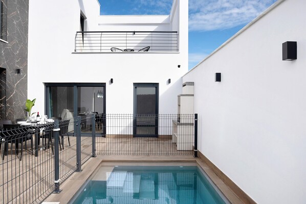 Un bâtiment moderne doté d’une piscine, d’un balcon avec des chaises et d’un coin repas aménagé avec du mobilier d’extérieur.