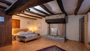 Une chambre à coucher avec un lit, des poutres en bois, une cheminée en pierre et un tapis rouge à motifs.