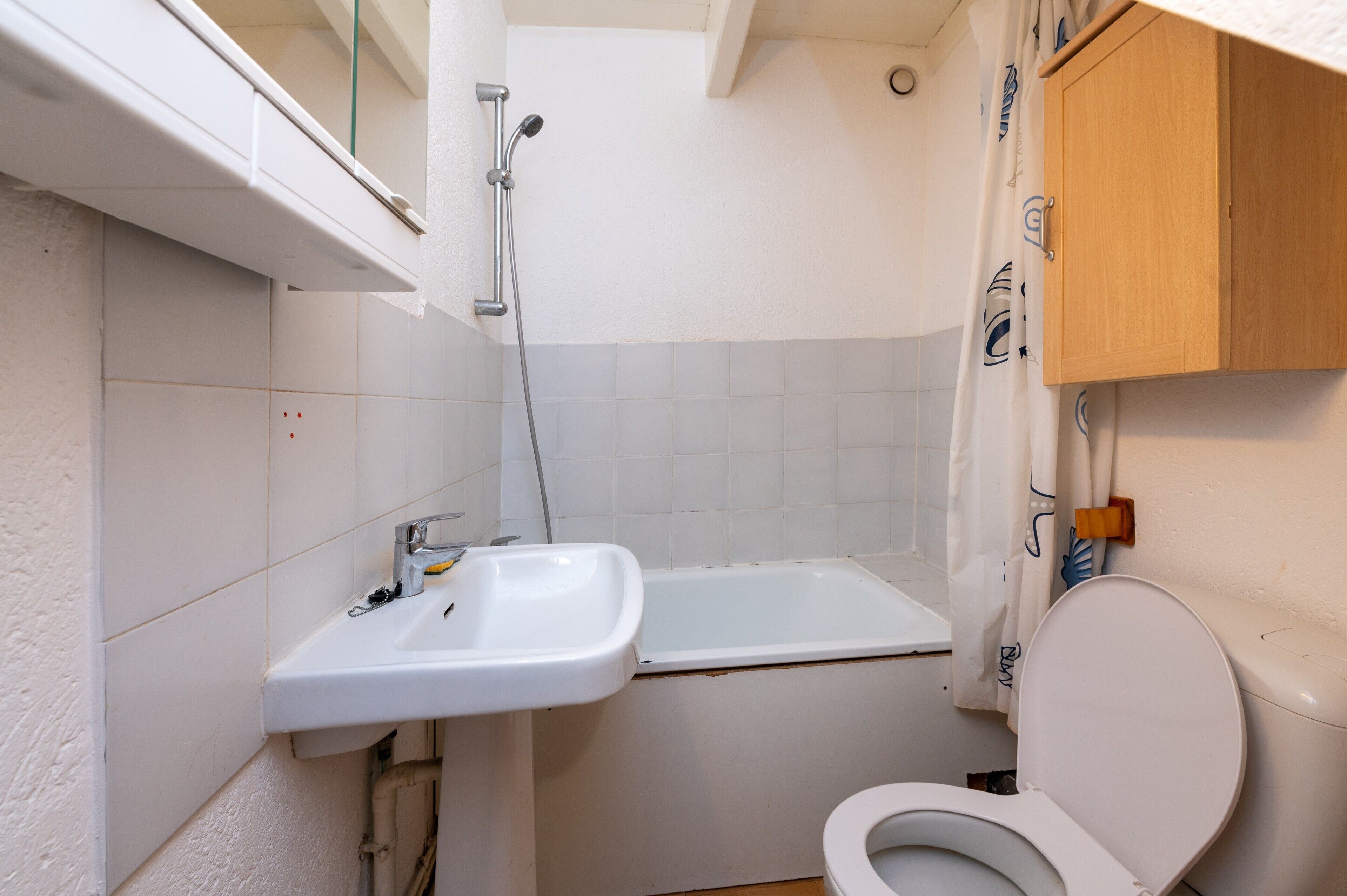 Une petite salle de bain avec un lavabo blanc, une baignoire et des toilettes.