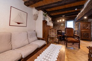 A cozy room with a sofa, wooden chairs, a table with a lace tablecloth, and a framed drawing on the wall.