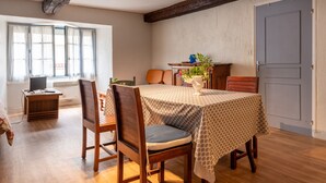 A dining area with a table set for two, wooden chairs, a small table with a plant, and a door in the background.