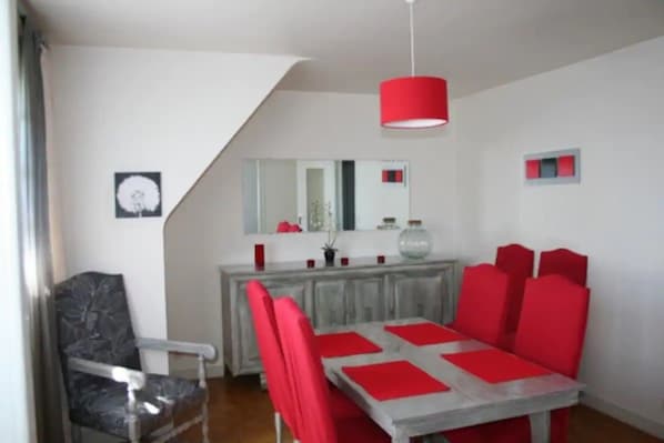 A dining area with a table and chairs, a red pendant light, a mirror, and a fish bowl on the counter.