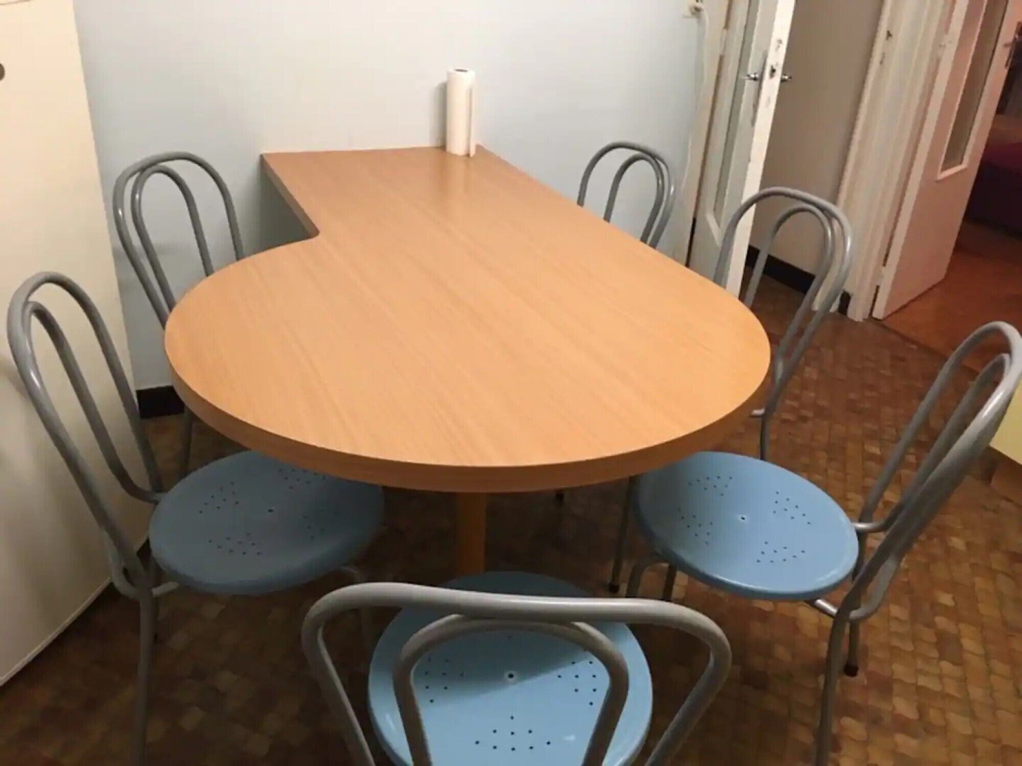 Una mesa redonda de madera con cuatro sillas de metal, una pared blanca y un suelo de baldosas.