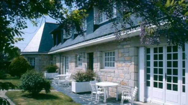 Een stenen huis met een overdekt terras en buitenmeubels.