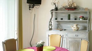 Een eetruimte met een ronde tafel, stoelen, een aan de muur bevestigde televisie en een decoratieve plank met decoratieve objecten.