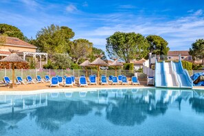 Ein Schwimmbecken mit blauen Liegestühlen, einer Rutsche und einem überdachten Bereich mit Sonnenschirmen.