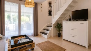 En moderne stue med trappe, fjernsyn, sofabord og en potteplante.