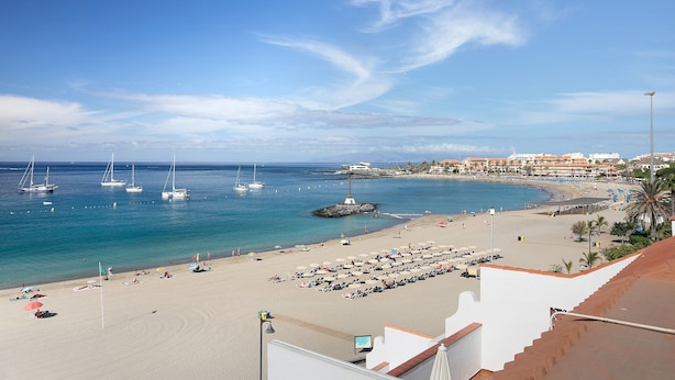 Una playa con barcos, sombrillas y un edificio al fondo.