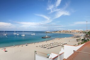 Une plage avec des bateaux, des parasols et un bâtiment en arrière-plan.