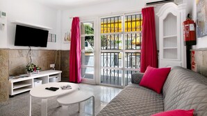 Una sala de estar con sofá, televisor, una mesita, una consola blanca y una ventana con cortinas.