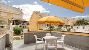 Un patio al aire libre con una mesa y sillas, una sombrilla amarilla y vistas a casas vecinas.
