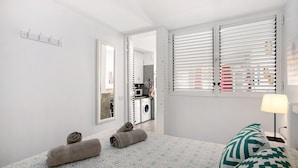 Un dormitorio con cama, toallas, una mesita de noche, lámpara y ventana con persianas.