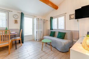 Una habitación acogedora con sofá, una mesita, una silla, televisor y ventana con cortinas.