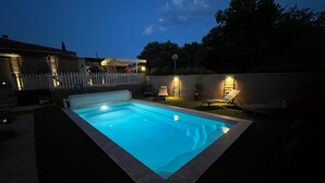 Ein rechteckiger Pool mit Fliesenrand, umgeben von einem weißen Zaun und einigen Liegestühlen.