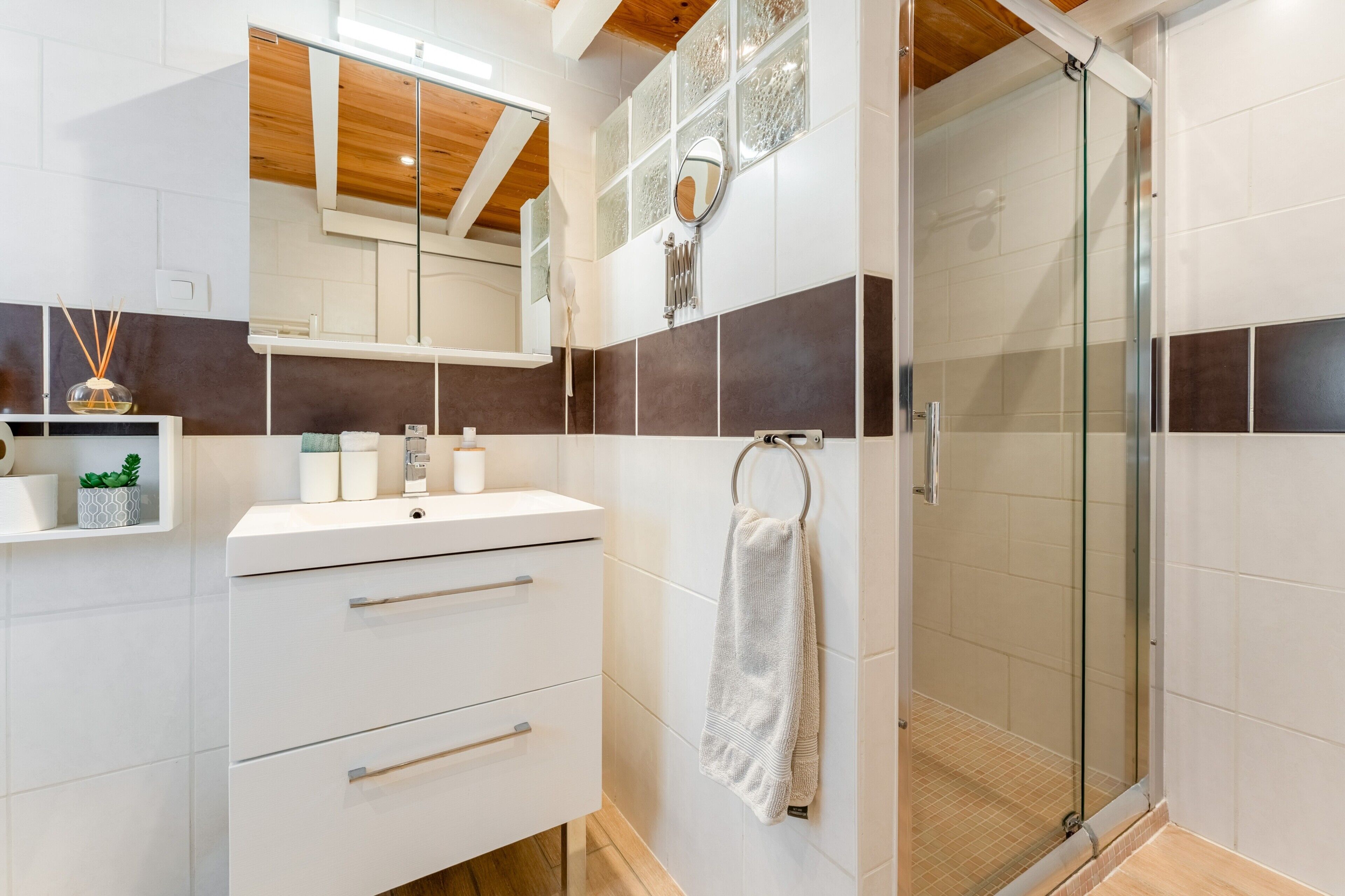 A modern bathroom with a glass shower enclosure, a white vanity with drawers, a mirror, and a towel rack.