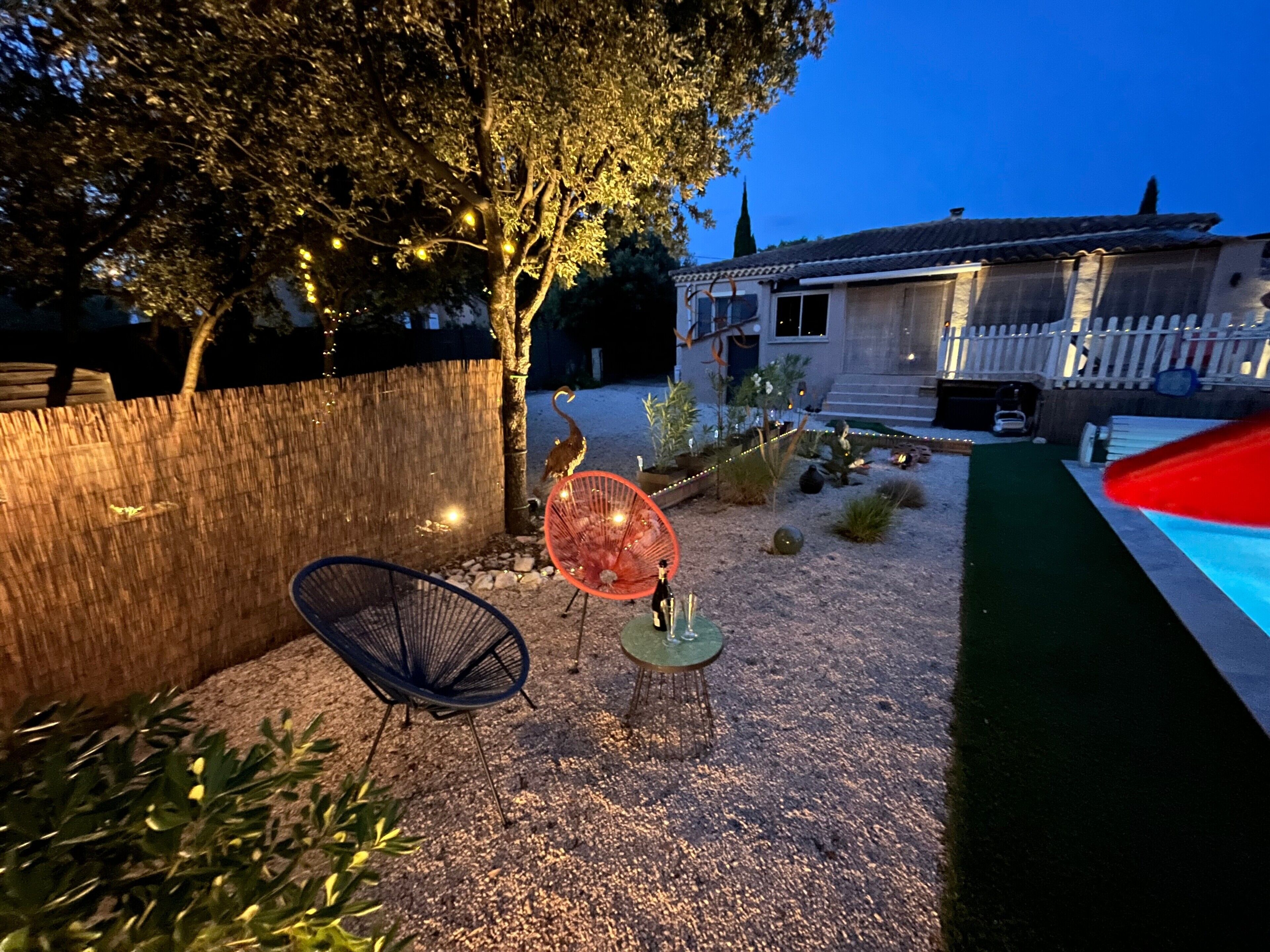A backyard with a wooden fence, a tree, a chair, a table, and a house in the background.