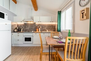 Una cocina moderna con armarios blancos, una mesa de comedor de madera y una cortina verde.