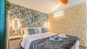 Ein modernes Schlafzimmer mit Wandverkleidung im geometrischen Muster, einer Steinwand, einem Bett mit dunkler Bettdecke und einem Nachttisch mit Lampe.