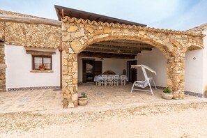 A stone archway leading to a patio with a table and chairs, surrounded by potted plants.