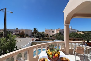 A balcony with a table set for breakfast, a pool, and buildings in the background.