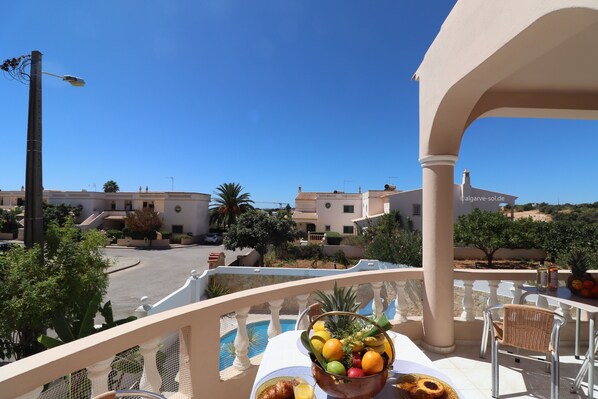 A balcony with a table set for breakfast, a pool, and buildings in the background.