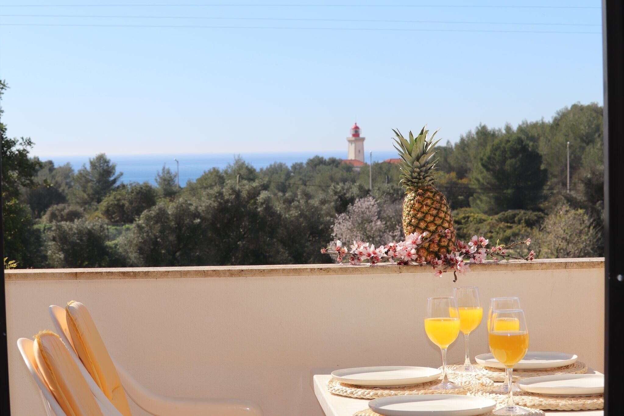 Ett bord med en ananas som mittpunkt, två glas apelsinjuice och en utsikt över en fyr och träd.
