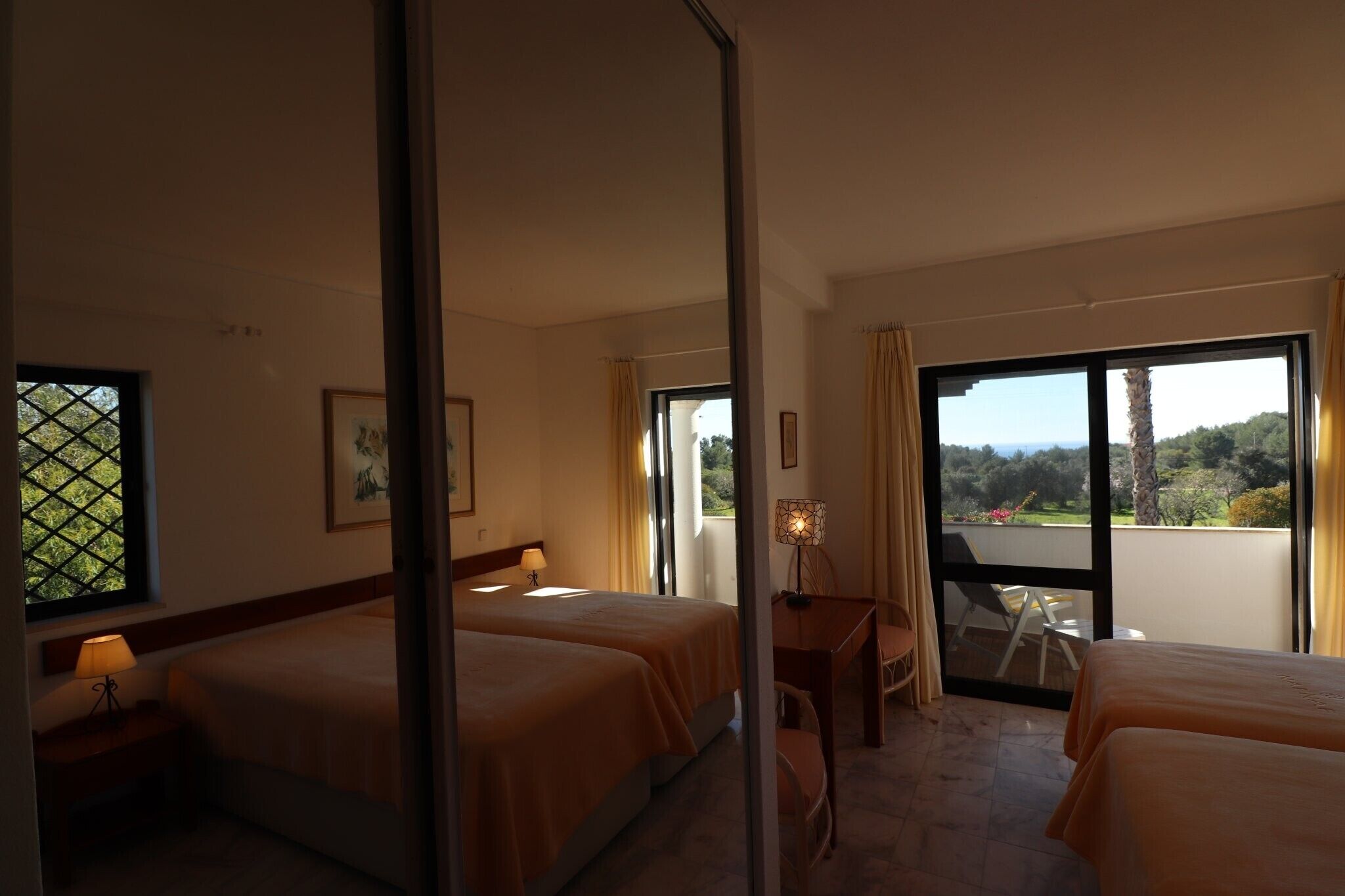 A hotel room with two beds, a desk, and a balcony with a view.