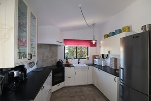 A kitchen with white cabinets, a black countertop, a stainless steel refrigerator, and a window with a view of greenery outside. - Villa 'La Perla' with Mountain View, Private Pool and Wi-Fi (Carvoeiro)