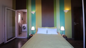 Une chambre à coucher avec un lit, deux lampes de chevet, un lave-linge dans la pièce adjacente et une porte.