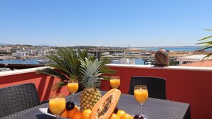 Une table avec des fruits et des boissons sur un balcon donnant sur une marina et sur la ville.