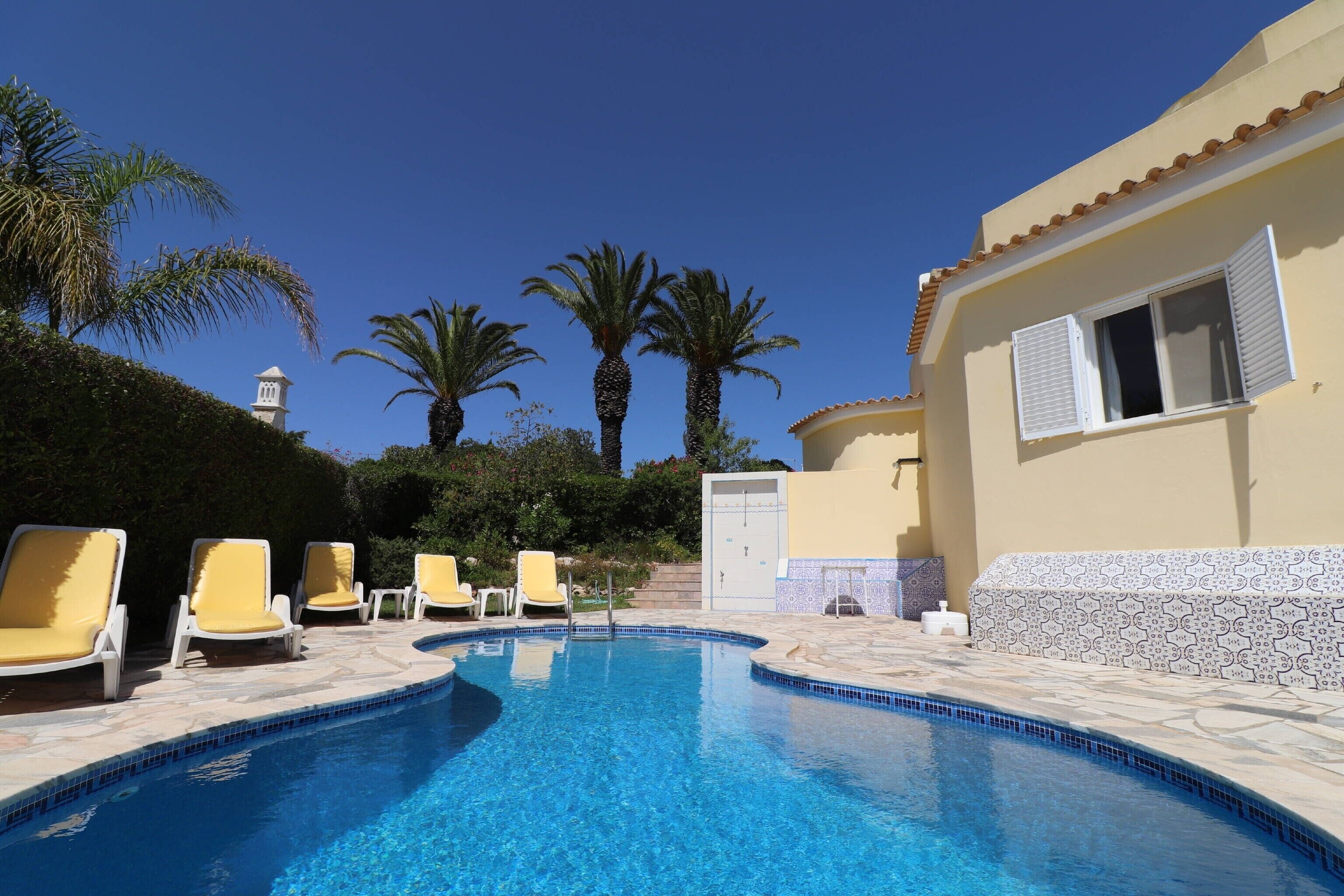 A swimming pool with lounge chairs, palm trees, and a building with a tiled roof.