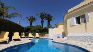 Ein Swimmingpool mit Liegestühlen, Palmen und einem Gebäude mit einem Ziegeldach.