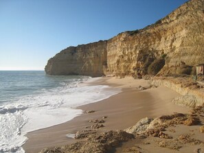 A beach with a rocky cliff and a wooden structure on the right.