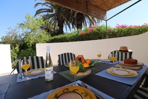 An outdoor dining table set with plates, cutlery, a bottle, and fruit.