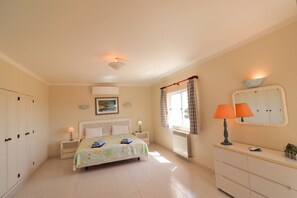 A bedroom with a bed, bedside tables, a dresser, a window with curtains, a radiator, and a ceiling light fixture.
