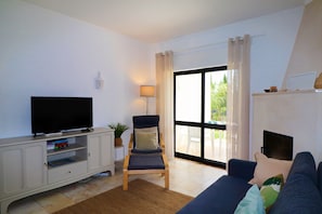 Ein Wohnzimmer mit Fernseher, einer Couch, einem Sessel und einem großen Fenster.
