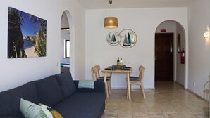 A living room with a sofa, a dining table with chairs, a pendant light, and a wall with a framed picture and decorative plates. - Apartment 'Casa Barbara' with Sea View, Shared Pool and Wi-Fi (Alporcinhos)