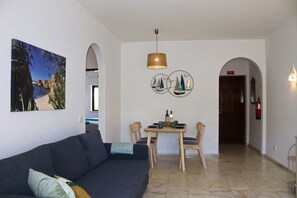A living room with a sofa, a dining table with chairs, a pendant light, and a wall with a framed picture and decorative plates.