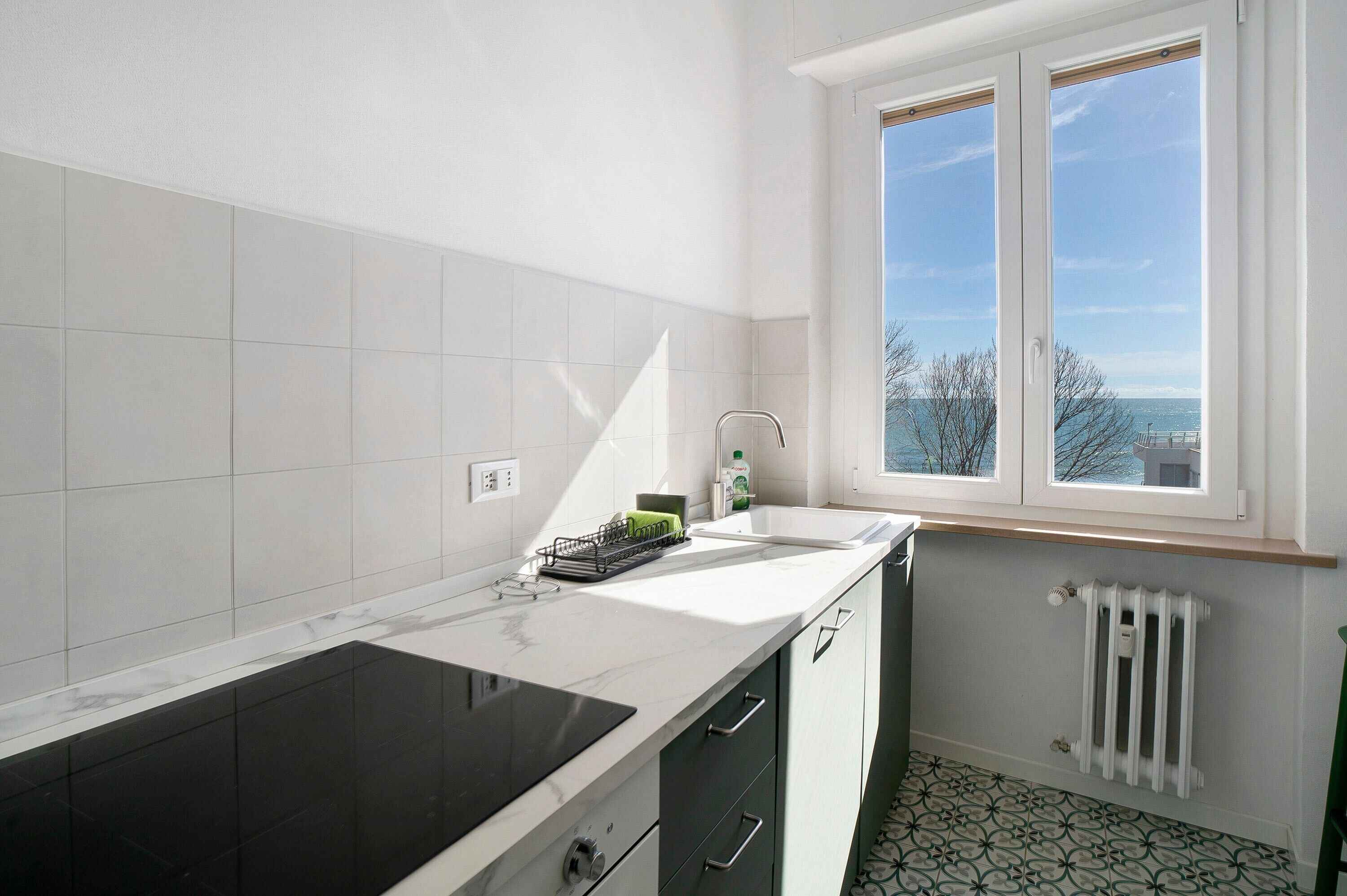 Une cuisine dotée d’une grande fenêtre, de carreaux blancs, d’un plan de travail noir et d’un radiateur.