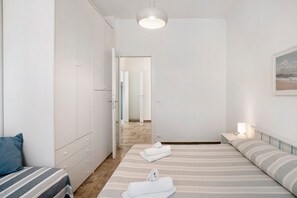 Un dormitorio con cama, armario, mesita de noche con lámpara y puerta que da a otra habitación.