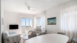 A modern living room with a round table, sofas, a flat-screen TV, and a painting. - Seafront Apartment 'Fronte Mare - Marina Di Andora' with Balcony, Wi-Fi & Air Conditioning (Marina di Andora)