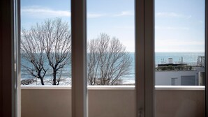 A view through a window with bare trees and a body of water in the background. - Seafront Apartment 'Fronte Mare - Marina Di Andora' with Balcony, Wi-Fi & Air Conditioning (Marina di Andora)